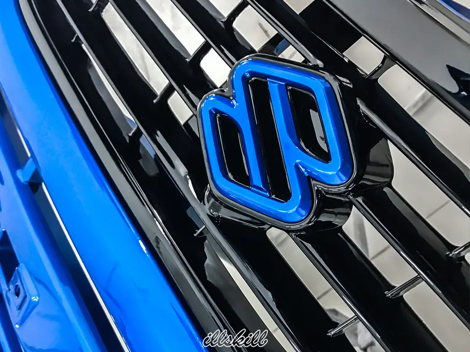 Синяя эмблема Suzuki на чёрной решётке