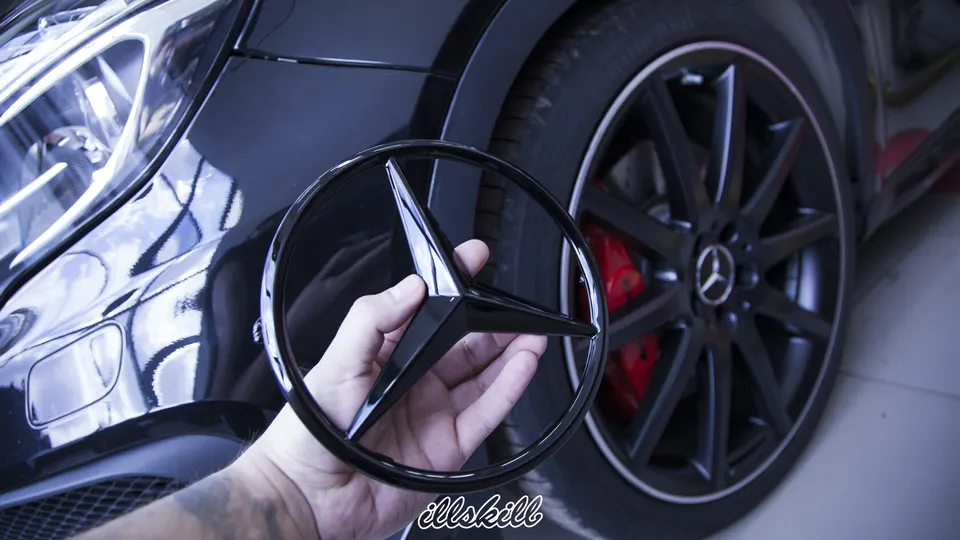 Чёрная эмблема Mercedes-Benz в руке рядом с автомобилем