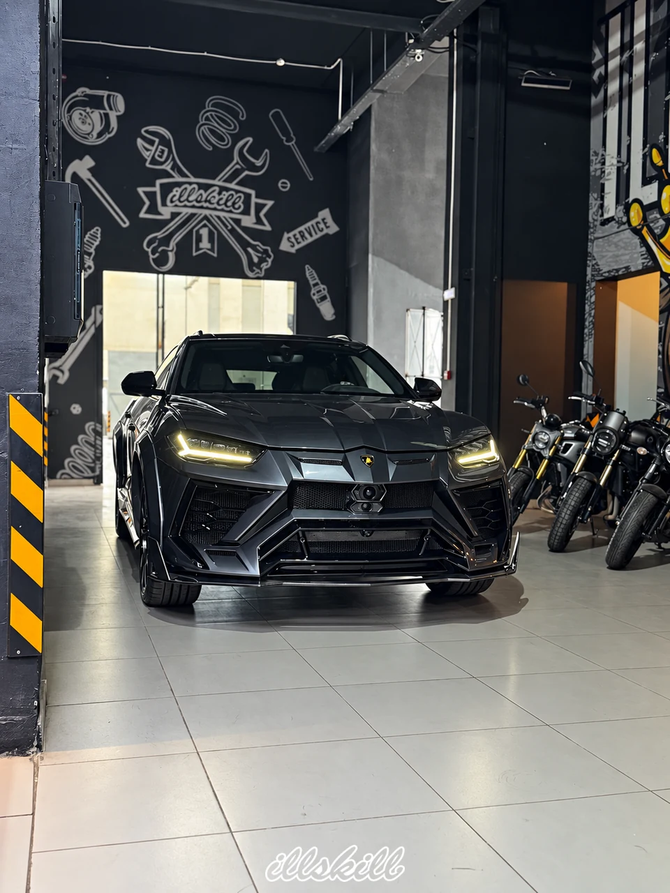 Lamborghini Urus в мастерской ILLSKILL, вид спереди с включёнными фарами. Фотография с согласованной ИИ-обработкой.