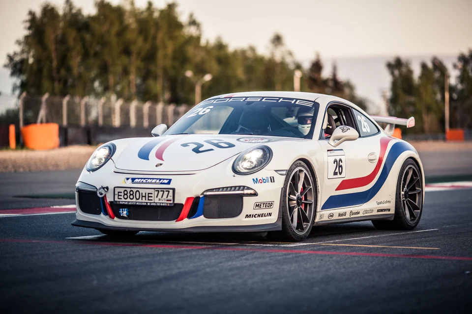 Белый Porsche 911 с красно-синими полосами на трассе, вид спереди