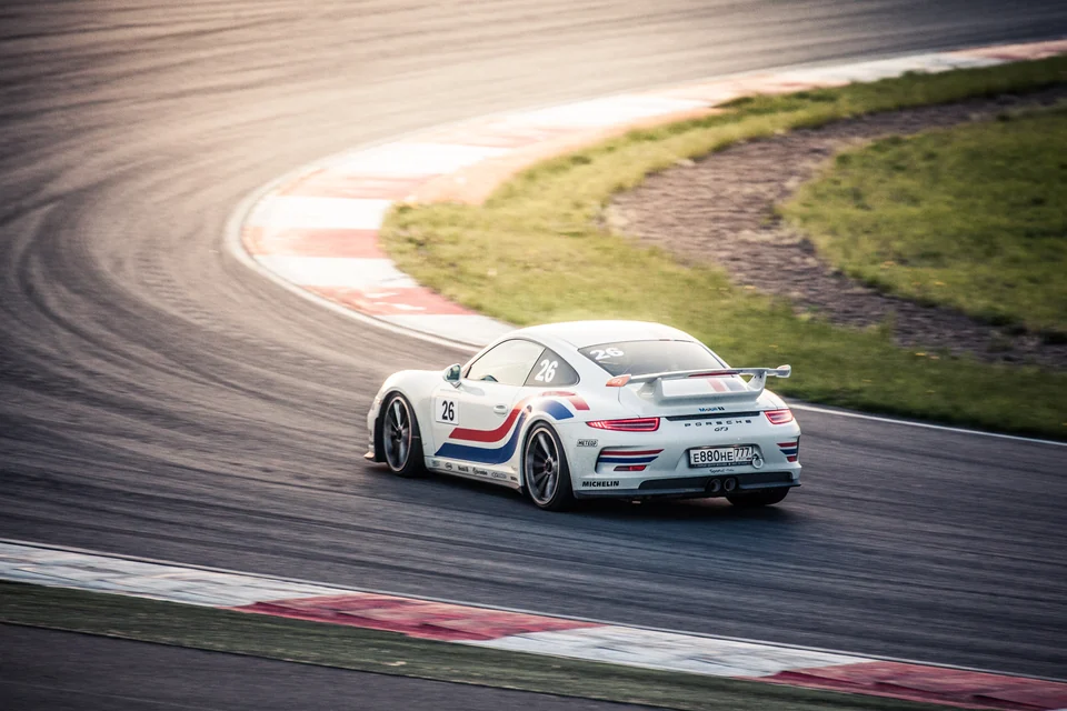 Белый Porsche 911 в повороте трассы, вид сзади
